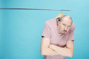 Funny bold man hanging on wooding clothes hanger over blue background.