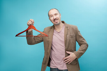 European man in brown jacket holding clothes racks over blue background with copy space.