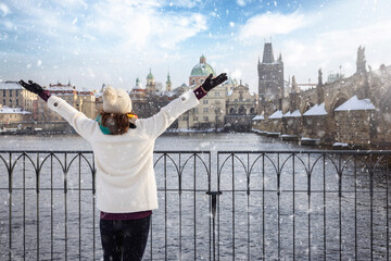 A happy tourist woman in winter clothing enjoys the view of the skyline of Prague with Charles...