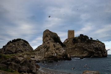 Fototapeta premium waves leading to big rocks and a stone tower