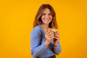 Portrait of woman eating a sandwich on a yellow background, healthy and vegetarian food