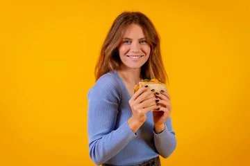 Selbstklebende Fototapeten Portrait of woman eating a sandwich on a yellow background, healthy and vegetarian food © unai