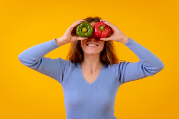 Vegetarian woman in a portrait with peppers in her eyes on a yellow background, healthy food