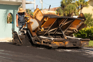 Cocoa Beach, Florida, USA, 2022. Asphalting worker applying tarmac from a asphalt paver machine to resurface a Florida driveway.