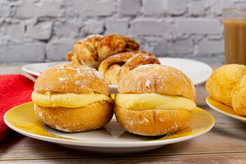 Table with Brazilian snacks. Cheese bread, sweet brioche, coffee with milk, and Berlin ball, a Brazilian donut called 