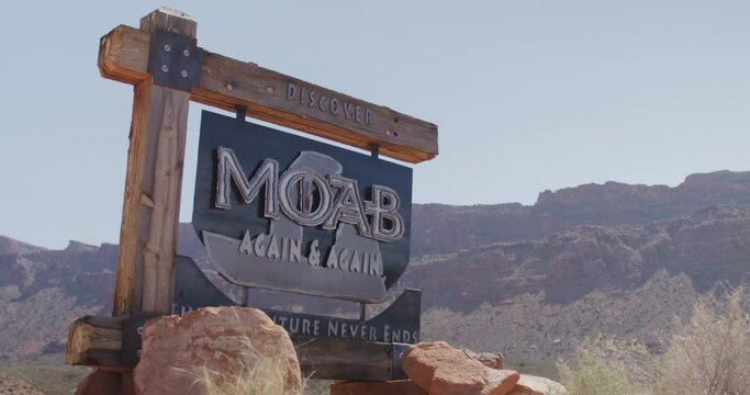 Panning on discover Moab sign in Utah with red cliffs in background on sunny day