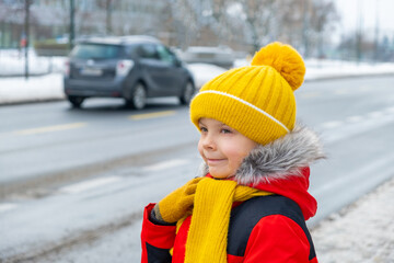 a boy stands in city near snow-covered road in winter.