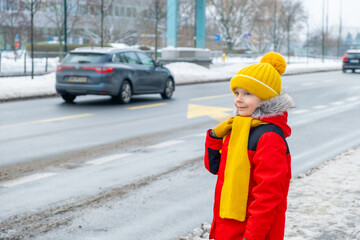 a boy stands in city near snow-covered road in winter.