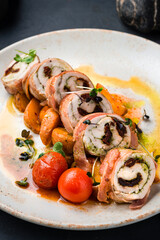 Lunch chicken rolls in bacon with pesto sauce and sun-dried tomatoes, closeup.