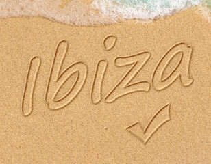 Simple Ibiza Spanish holiday getaway message written in smooth sand with an incoming wave on a tropical beach