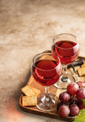 Two glasses of red wine, a bunch of red grapes, crackers and corkscrew on a wooden tray on beige textured background with text space. Celebration party for two concept