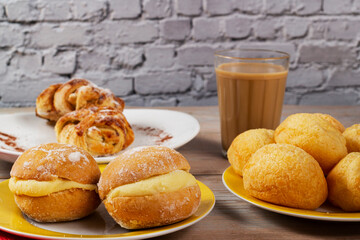 Table with Brazilian snacks. Cheese bread, sweet brioche, coffee with milk, and Berlin ball, a Brazilian donut called 