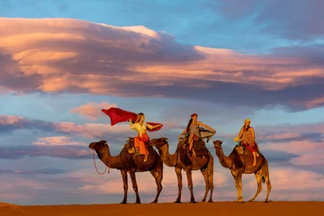 Gartenposter Three Riders And Their Handler Travel Through The Saharan Desert On Their Camels In Morocco © Grindstone Media Grp
