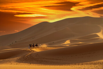 Fototapeta na wymiar Three Riders And Their Handler Travel Through The Saharan Desert On Their Camels In Morocco