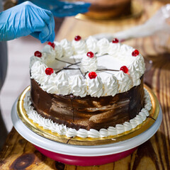 Young woman chef decorating cake with cherrys. Small baking business.