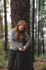 portrait of a woman with a mobile phone next to a tree in the middle of the forest with a pink jacket and brown hair
