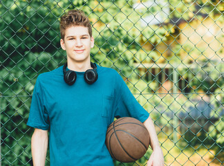 Cute young teenager in t shirt with a ball plays basketball on court. Teenager running in the...