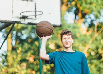 Cute young teenager in t shirt with a ball plays basketball on court. Teenager running in the stadium. Sports, hobby, active lifestyle for boys