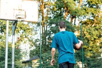 Cute young teenager in t shirt with a ball plays basketball on court. Teenager running in the stadium. Sports, hobby, active lifestyle for boys