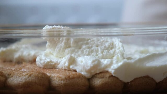 the process of cooking tiramisu. the cook lays out and smears mascarpone on the rows of savoiardi, ladyfinger (biscuit), sponge fingers, boudoirs, baby fingers. mascarpone in tiramisu