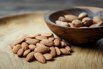 Peeled raw almonds on a wooden plate and almonds in a shell in a wooden bowl on a wooden background.