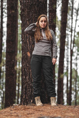 brown-haired caucasian girl next to a tree in the middle of the forest