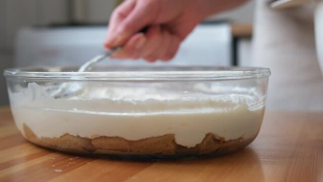 the process of cooking tiramisu. the cook lays out and smears mascarpone on the rows of savoiardi, ladyfinger (biscuit), sponge fingers, boudoirs, baby fingers. mascarpone in tiramisu