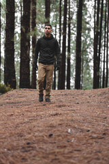 boy with black hair in the middle of the forest looking up at the trees and walking