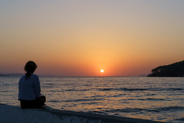 Silhouette of a man at sunset. Evening landscape with a lonely man on the seashore, looking at the sunset and the sky. Loneliness, calmness, sadness emotions.