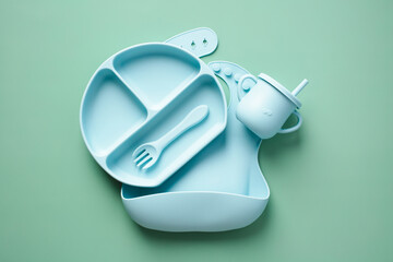 Baby silicone tableware set on color background. Flat lay bowl, plate, fork, baby bip. Top view.