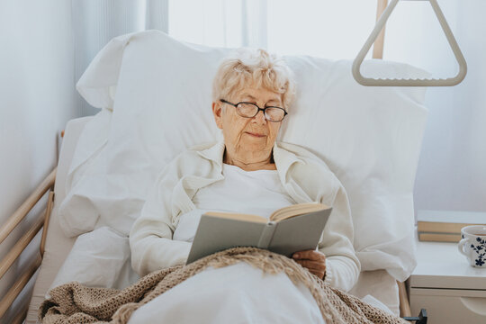 Sick senior woman lies in a hospital bed and reads a book