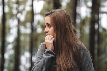 girl with brown hair in the middle of the forest being cold