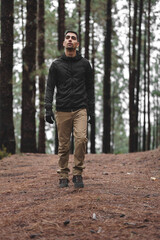 boy with black hair in the middle of the forest looking up at the trees and walking