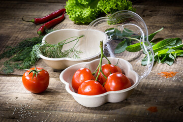 A branch of tomatoes in an eco-friendly disposable container on wooden background