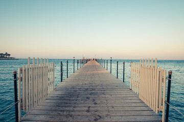 Obraz premium Wooden pier at sunrise in the tropical sea. Palm trees in the distance. Beautiful wooden pier. Long exposure of the sea as a haze