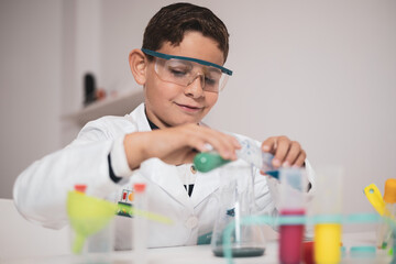 Boy having fun with chemistry lab in his living room. Science experiments at home for school homework. The little one is wearing goggles and a white coat.