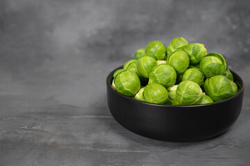 Black bowl with fresh Brussels cabbage on gray concrete background.