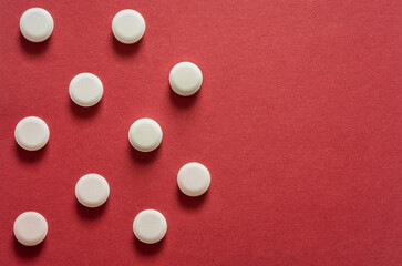 small round white pills, lots of little tablets on red background close up. Simple group of little pills, medicine