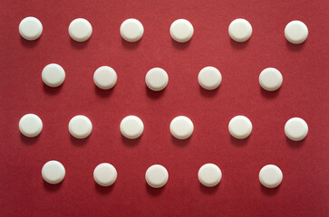 small round white pills, lots of little tablets on red background close up. Simple group of little pills, medicine
