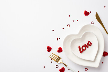 Valentine's Day concept. Top view photo of heart shaped plates with inscription love knife fork and confetti on isolated white background with copyspace