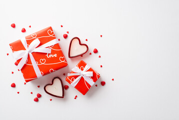 St Valentine's Day concept. Top view photo of red gift boxes with silk ribbon bows heart shaped candles and sprinkles on isolated white background