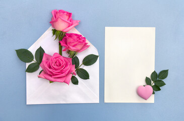 Pink flowers roses postal envelope with paper card note with space for text, pink heart on a blue background. Top view, flat lay