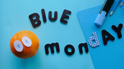Letras de BLUE MONDAY en un fondo azul con una naranja con ojos y material de papelería azul