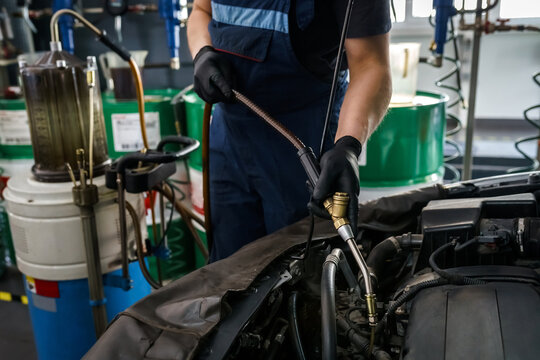 Male mechanic in a protective suit changes the oil in a car engine in a car service garage. Car maintenance and repair