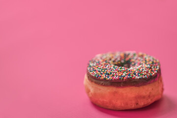 Fototapeta na wymiar Chocolate Donut with Rainbow Sprinkles on Pink Background