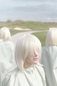 Conceptual portrait of unrecognizable young pale woman with white blonde hair standing outdoors, long fringe covering her face  