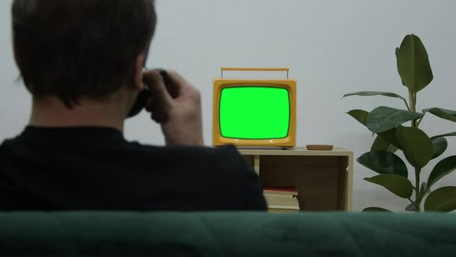 A man is watching an old tube TV sitting on the so