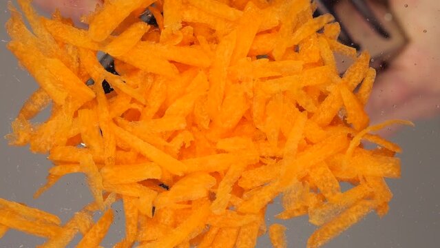 The cook rubs raw carrots into a glass dish. Bottom