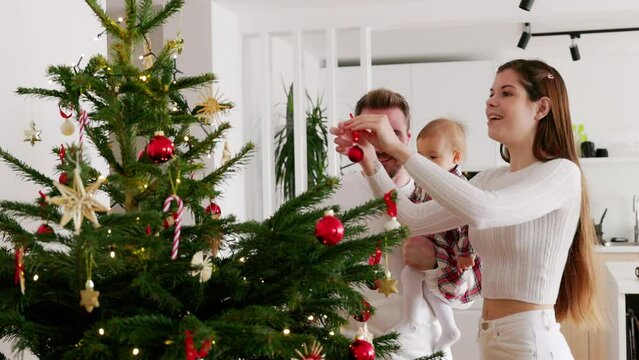 Young family of three decorating the Christmas tree in their new home