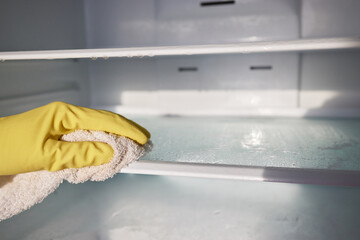 Woman cleaning empty refrigerator with rag, closeup.